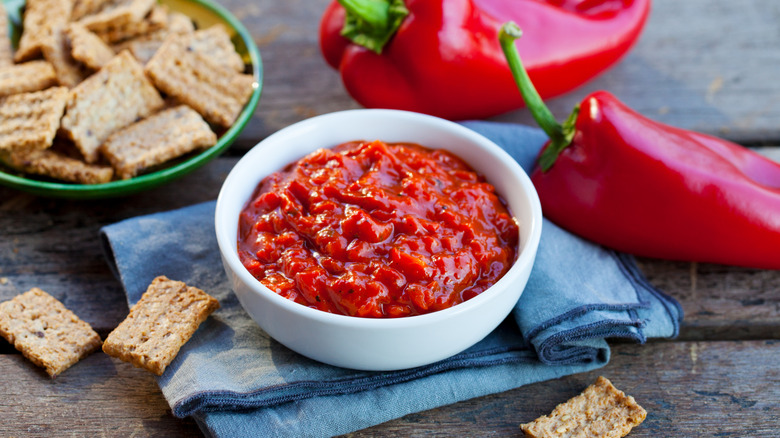 bowl of pindjur on a blue napkin with red peppers and crackers