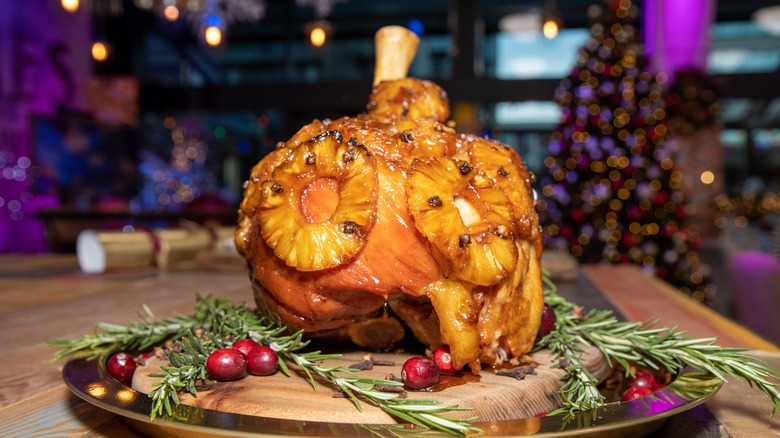 glazed ham with pineapple rings on a round wooden plate decorated with pine needles and red berries