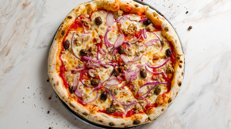 Pizza with tuna, olives, and onions on a plate resting on a marble countertop