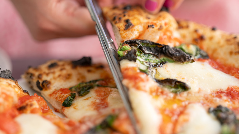 Hand using scissors to cut pizza