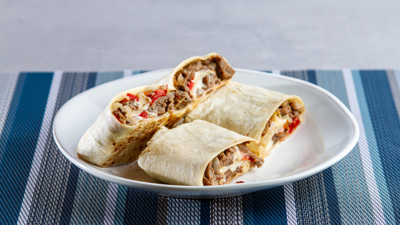 A plate holding two burritos cut in half on a placemat