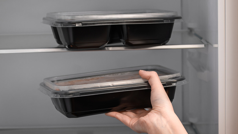 a hand placing a black plastic takeout container in the refrigerator