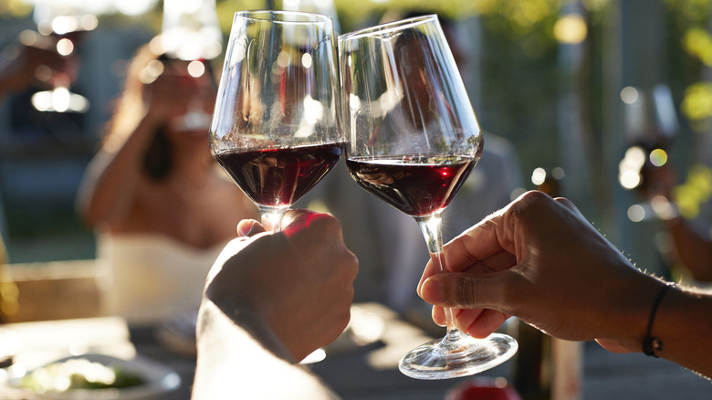 Two people toasting with glasses of red wine at a table with friends