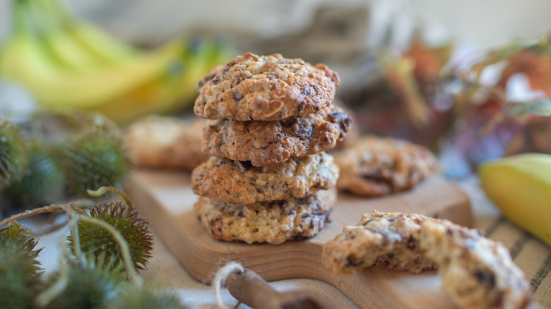 A stack of banana chocolate chip cookies on a cutting board surrounded by bananas