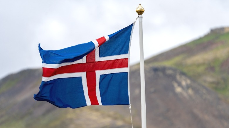 The Icelandic flag flying in front of a hill.