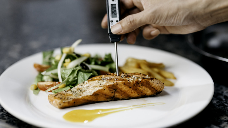 Person's hand checking the internal temperature of salmon with a thermometer stick