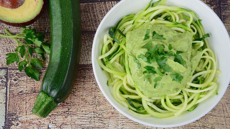 a bowl of pesto-topped zoodles with zucchini and avocado