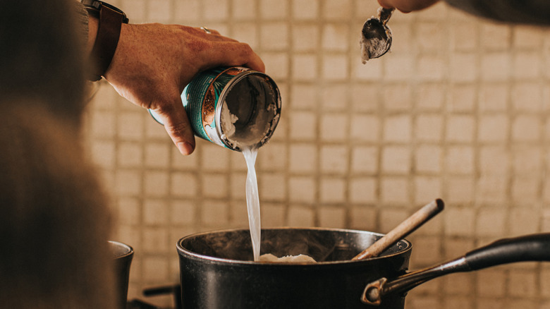 pouring can of coconut milk into pot on stovetop