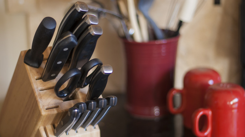 Knives in a wooden knife block next to some red mugs