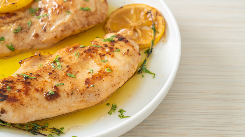 Baked chicken breasts on a plate with lemon and herbs