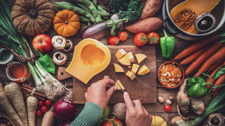 Someone cutting up a butternut squash with other autumn vegetables on the table