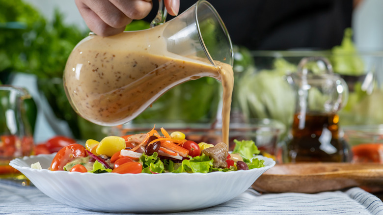 Pouring vinaigrette from glass pitcher onto salad