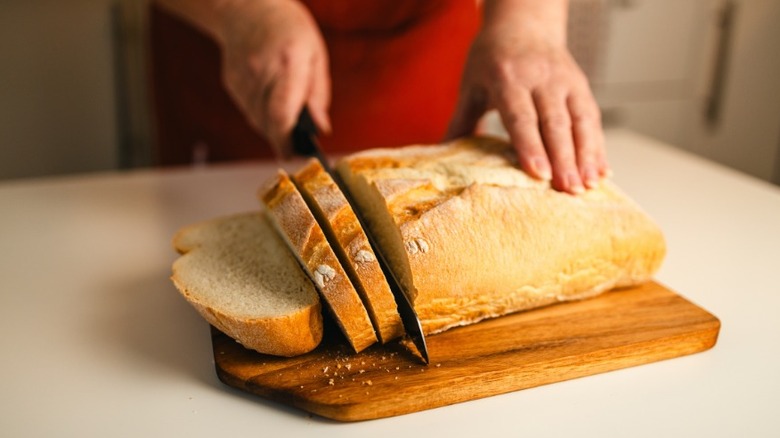 Fresh bread being cut into slices on wooden cutting board