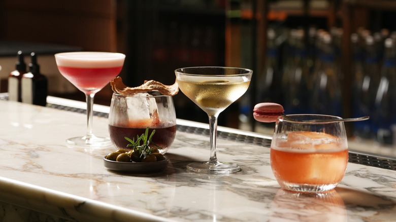 A selection of cocktails and a small plate of olives on a marble bar counter