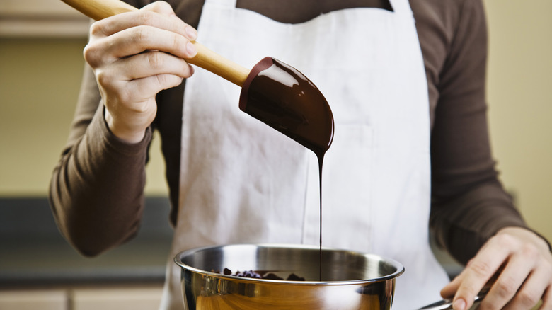 A person melting dark chocolate over a metal bowl