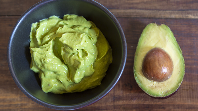 Puréed avocado in bowl with cut avocado