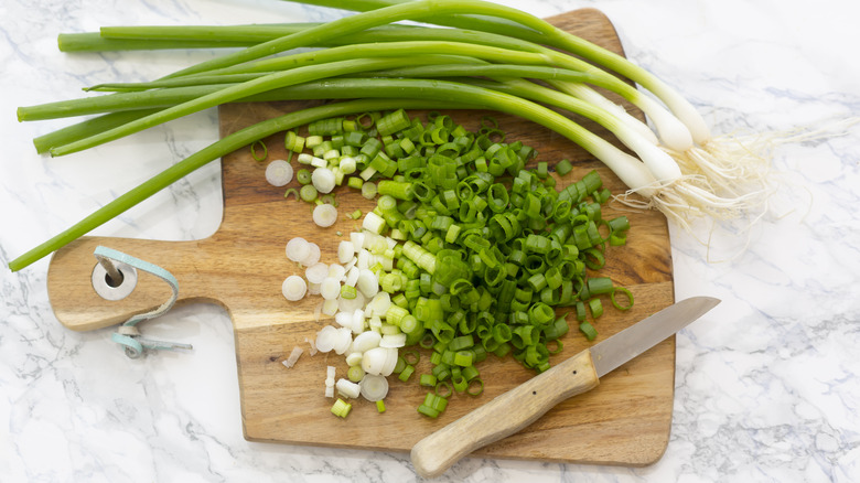 Chopped and whole scallions on wooden board