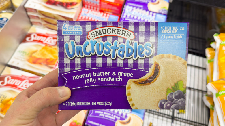 A hand holding an Uncrustables package over other freezer items