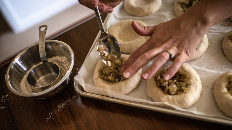 Hands filling bialys on baking sheet