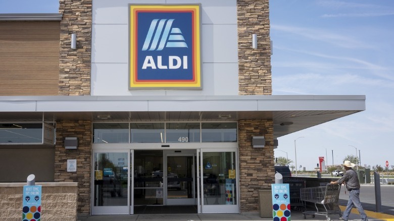 Man walking cart into an Aldi store.