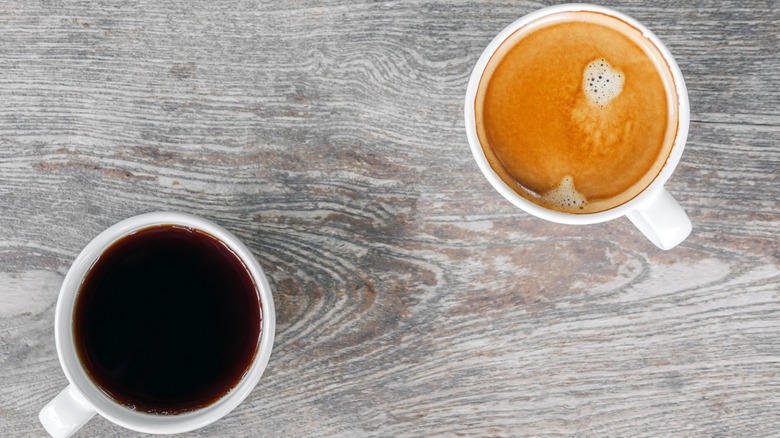 Two mugs of coffee side by side on grey wood