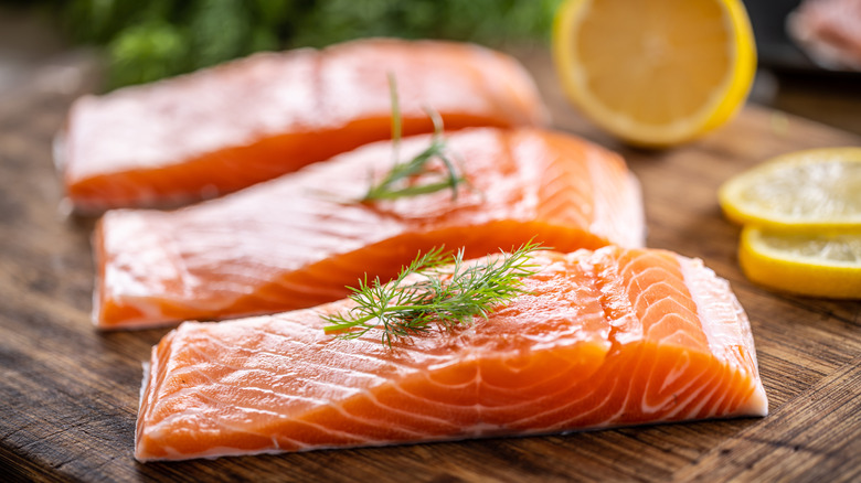 Three raw salmon filets on wood board with dill and lemon