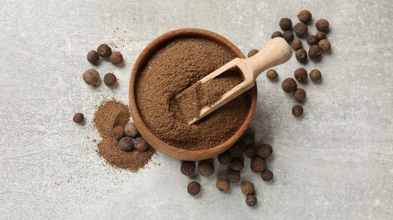 Top view of ground allspice in a wooden bowl with whole allspice around the bowl