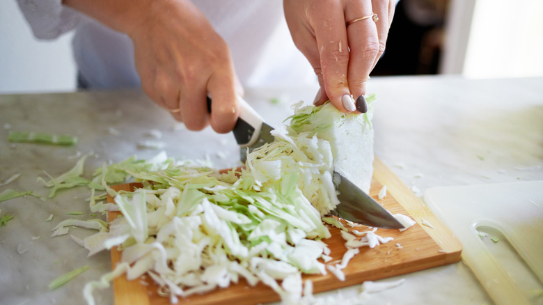 A woman cutting cabbage on a wooden cutting board