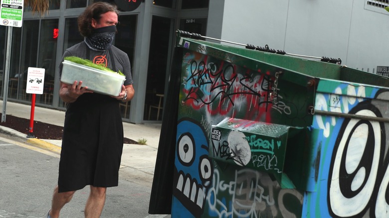 Restaurant worker throws raw vegetables into a dumpster