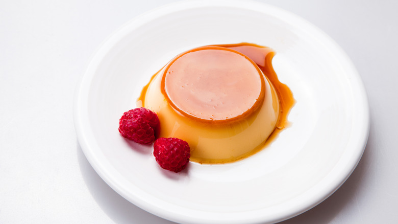 A flan on a plate with two raspberries