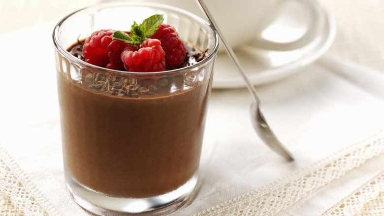 A chocolate pudding in a glass cup topped with raspberries