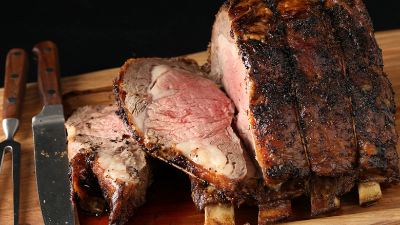 Slices of bone-in prime rib being cut on a wooden cutting board