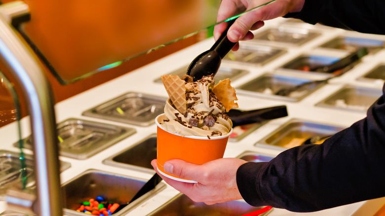 man adding toppings to frozen yogurt cup