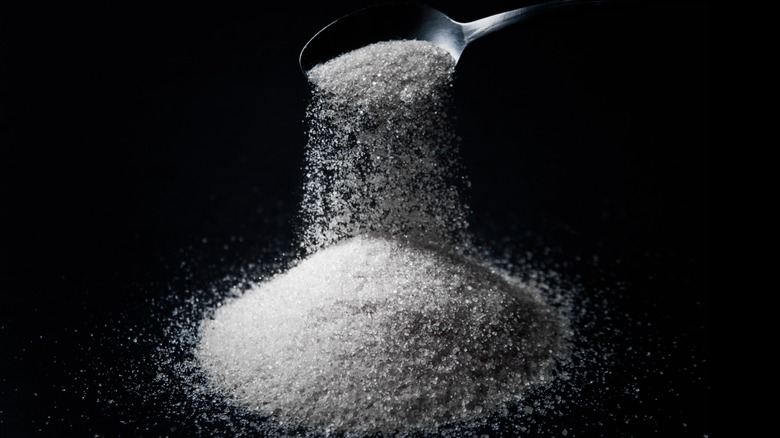 Adding to a pile of granulated sugar with a spoon