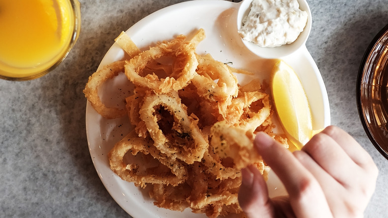 Fried calamari on a white plate with sliced lemon and dipping sauce