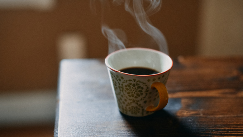 a mug of steaming coffee sitting on a wooden surface