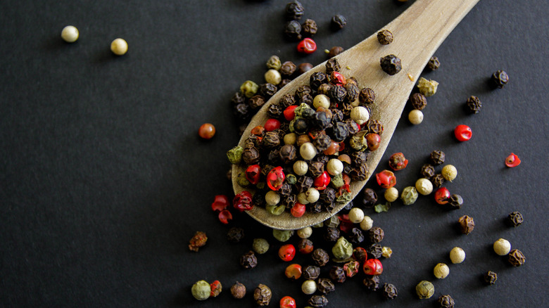 A wooden spoon with a variety of colorful peppercorns