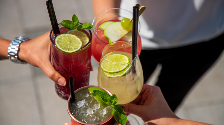 Four people toasting cocktails with lime and mint garnish