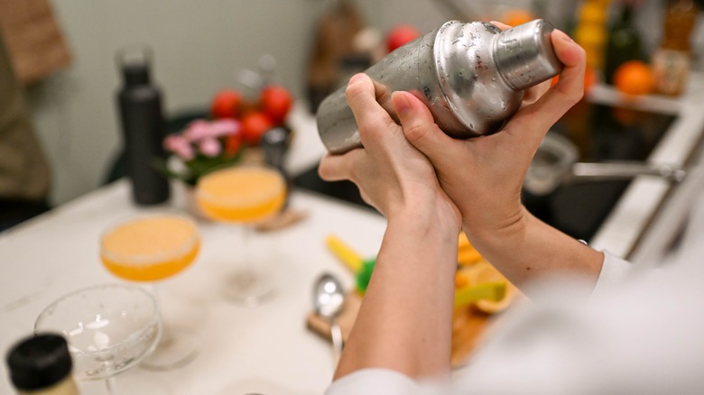 Holding a cocktail shaker over a kitchen table with drinks