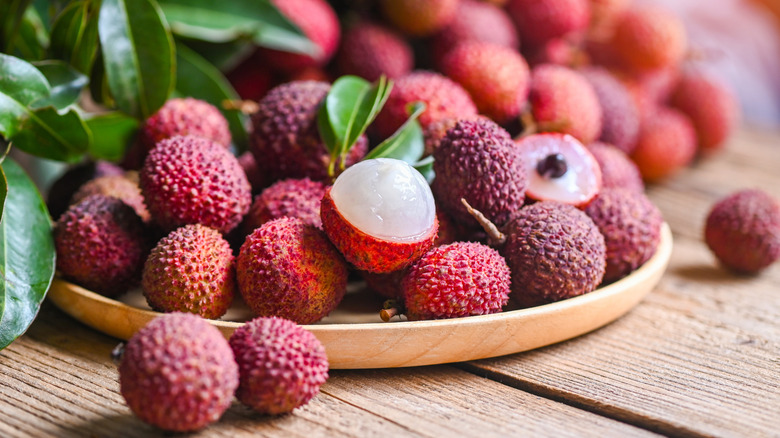 A bowl of fresh lychees with one half-peeled lychee on top