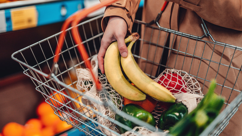 person placing bananas in shopping basket with other produce