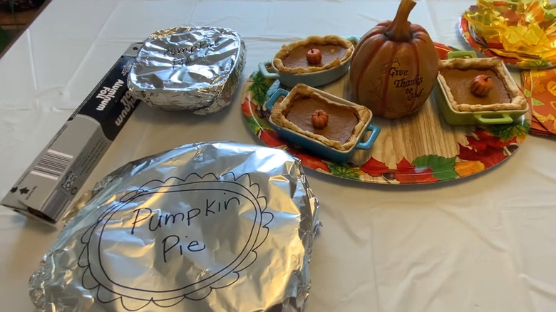 Foil-wrapped pumpkin pie on a table next to decoration