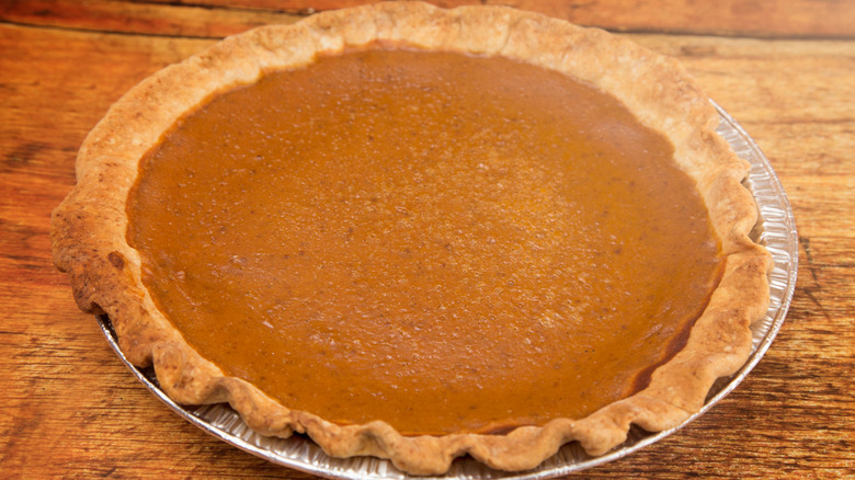 Close up of a pumpkin pie in its tin on a wood surface