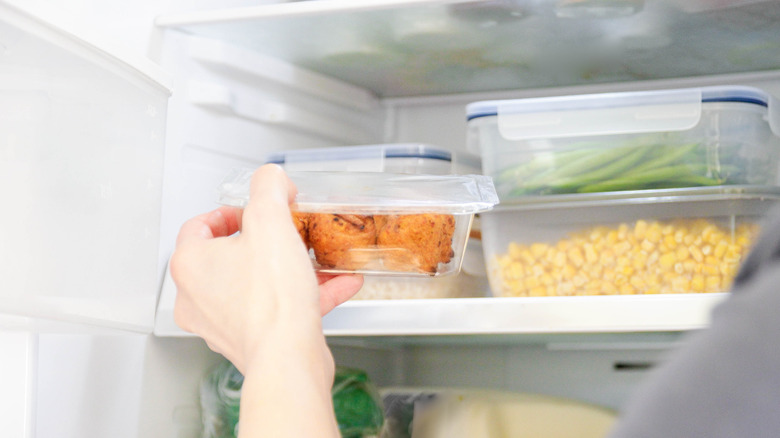 An arm grabbing a container with food out of a refrigerator