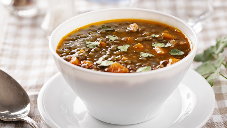 A bowl of stew, including lentil and carrots sitting on a table.