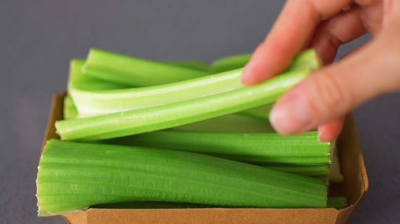 A hand picks up a celery baton from a pile of cut celery