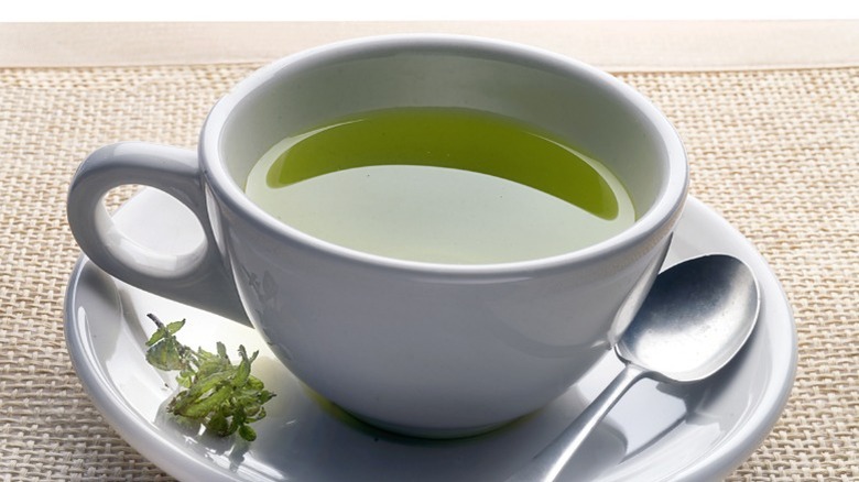 A cup of green tea in a saucer with a spoon and garnish