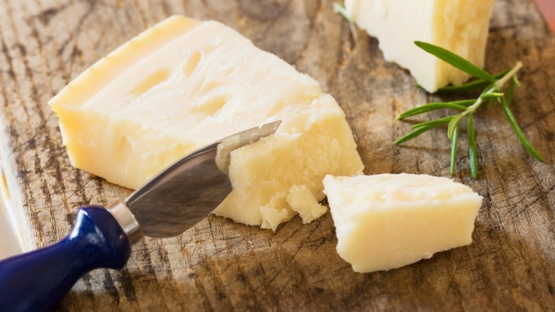 A wedge of parmesan on a wooden cutting board with a knife