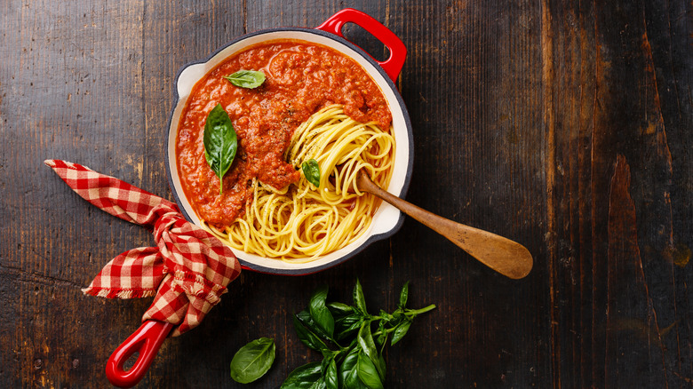 Spaghetti noodles and bolognese sauce in a red cooking pot with a handle