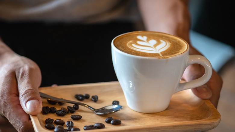 A person carrying a tray with a latte on it.